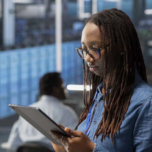 Engineer in server room using tablet to implement and manage data backup solutions to protect against data loss and ensuring efficient recovery processes, identifying and resolving technical issues